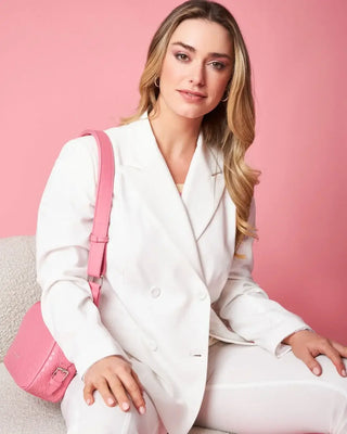 Woman in a white suit with a pink handbag, showcasing elegant fashion accessories from Accessori Outlet against a pink backdrop.