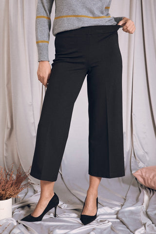 Pantaloni cropped neri comodi con vita elastica, indossati con un maglione grigio, perfetti per ogni occasione elegante.