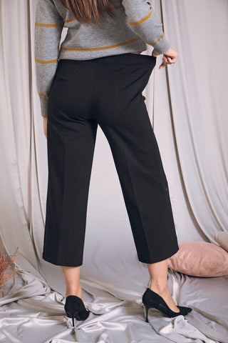 Donna che indossa pantalone cropped nero con vita elastica, mostrando il retro, abbinato a un pullover grigio.