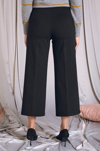 Pantaloni cropped neri con vita elastica, gamba a culotte, indossati con scarpe eleganti su sfondo di tessuto morbido.